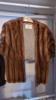 Full view of brown fur stole hanging on wooden hanger showing fur texture and length.