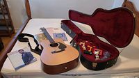 Overview of guitar, strap, books and open case with accessories