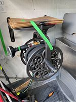 Side view of decorative metal hose reel with garden hose and attached spray nozzle, mounted on wall with metal bracket