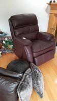 Front view of brown leather recliner, shows padding, seat cushion and visible toss cushions and ottoman in foreground