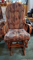 Front view of wooden rocker glider chair upholstered in patterned fabric in shades of brown and beige.