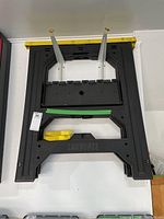 Two black plastic sawhorses stacked, show top view with yellow rail caps and white metal braces.