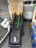 Stack of 17 black folding chairs in front of folded table top.