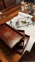 Photo showing four trays: a hand-painted glass tray with wire rack and a set of three nested wooden trays with carved inlay placed on a wooden table.
