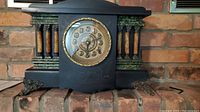 Front view of the entire vintage black mantel clock with decorative gold-tone dial and key.