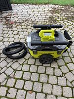 Front and side view of Ryobi cordless wet/dry vacuum with hose and wands coiled beside it