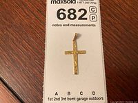 Gold cross pendant resting on a white lot card showing front with engraved floral and vine design.