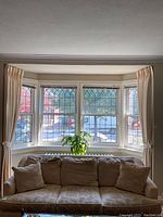 Four cream pinch pleat panels hung on bay window, two tied back, showing full drape and color.