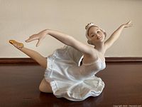Full side view of antique German bisque ballerina figurine showing delicate white tutu, extended arms and gold ballet shoes.