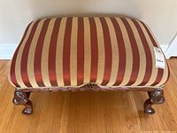 Top view of footstool showing striped burgundy and cream fabric upholstery and carved wooden frame with cabriole legs.