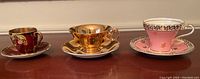 Front view of three vintage Aynsley tea cups and saucers on a wooden surface.