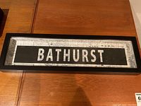 Framed shadow box style artwork featuring the Bathurst street name in white letters on black with map background, placed on a wooden surface.