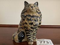 Front view of the glazed ceramic calico cat figurine with detailed stripes, green eyes, and lifelike expression.