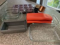 Overview of all bakeware and kitchen accessories arranged on countertop including glass and metal bakeware, silicone mitts, bowls and measuring cups