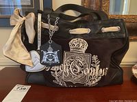 Front view of tote bag showing embroidered crest, handles, scarf accent and charm.