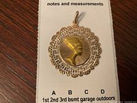 Front view on white card showing raised Nefertiti profile and Greek key scalloped border