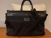 Front view of black Oscar de la Renta overnight bag with cream pillow behind