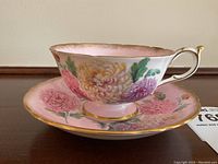 Side view of the teacup set on saucer showing floral pattern and gold trim