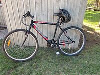 Side view of the Supercycle men's mountain bike, black frame with red and gray detailing, helmet mounted on seat post