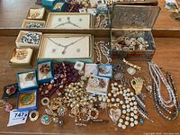 Overall lot view of assorted necklaces, brooches, earrings, rings and beads laid out on wooden surface