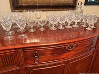 Full display of crystal wine glasses arranged on wood sideboard with crystal decanter at the right end, showing variety of glass sizes and patterns.