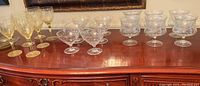 Overview of lot showing six yellow wine goblets, ten clear dessert coupes and six clear shrimp cocktail servers arranged on wood sideboard