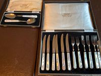 Overview of two boxed sets: one with knives and forks, the other with serving spoon and ladle, all with mother of pearl handles.