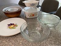Overview of all items showing Pyrex bowls, Corning Ware casserole with floral pattern, Duralex glass bowls, and Thomas platter with fruit design.