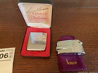 Photo of two vintage Ronson lighters; one inside green and red lined box marked 'Vaporflame Banker by Ronson,' the other resting on a maroon felt sleeve embroidered with 'Ronson'. Both lighters are silver-tone metal with engraved lines.