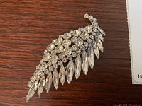 Clear image of the Sherman rhinestone leaf brooch laid flat on a wooden surface showing detail of stones and shape.