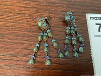Both earrings laid flat on wooden surface showing their full length, turquoise stones, and enamel flower details.
