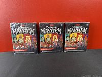 Three new sealed packs of Dungeons & Dragons Dungeon Mayhem card game placed in a row in front of a red background.