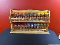 Front view of the wooden spice rack with all 20 glass bottles visible, showing various colored lids arranged in two rows behind wooden rods.