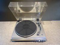 Turntable open with dust cover raised showing platter, tonearm, and control buttons.