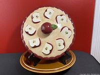 Front view showing the ceramic dish with the decorative apple pie slice lid and central apple handle.