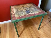 Side angled view of the vintage card table showing wear and folding leg design.