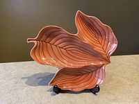 Front angle of the orange leaf-shaped dish with black vein details displayed on stand.