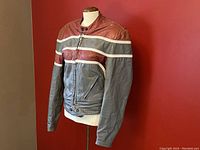 Full sleeve front view of vintage motorcycle leather jacket on mannequin against red wall showing large zipper, snap button on collar, and pocket zippers.