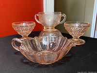 Six pieces of vintage pink depression glass dessert ware displayed together showing variety of bowl shapes and textures.