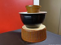 Three stacked ceramic stoneware bowls including small brown, medium ribbed brown, and large black and white bowl