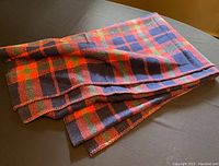 Folded vintage tartan blanket with visible red, blue, and green plaid pattern on dark fabric surface.