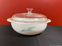 Front and side view of the white opaque glass Pyrex casserole dish with turquoise wheat design and clear glass lid.