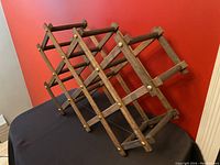 Perspective view of vintage wood accordion style expandable wine rack on black surface against red wall.