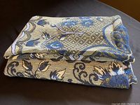 Folded knit blanket showing the contrasting blue floral design on one side and yellow floral design on the other, highlighting the double-sided pattern and knit texture.