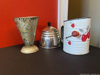 Photo showing the set of three vintage kitchen items with measuring cup, honey pot and flour sifter positioned from left to right.