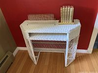 Front view of the white wicker vanity table showing the woven top, shelf underneath, and decorative lattice sides.
