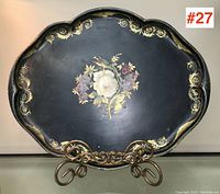 Full view of black painted tole tray with floral center and gold scroll borders on metal ornamental stand