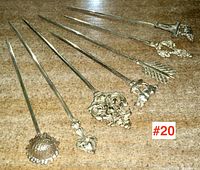 Seven antique/vintage metal game skewers laid side by side on a wooden surface, each with a unique ornate or figural handle design, sizes approximately 8 to 10 inches long.