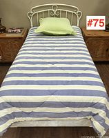 Full view of single bed with striped bedding and white metal headboard, showing assembled bed and two bedside tables.
