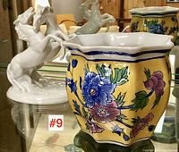Front view of yellow flower pot with blue and pink flowers and white horse figurine in background
